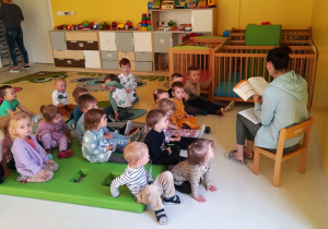 Dzieci na dywanie słuchają czytanego przez opiekunkę wiersza.