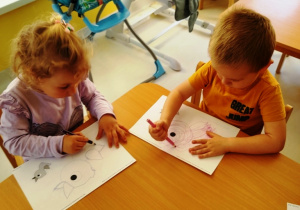 Dzieci przy stoliku rysują po śladzie ptaszka.