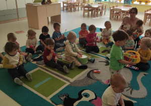 Zdjęcie dzieci siedzących na dywanie podczas wspólnego grania na instrumentach muzycznych do piosenki ,,Jestem Muzykantem''.