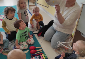 Opiekunka pokazuje dzieciom instrument noszący nazwę: Trójkąt.