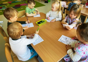 Dzieci siedzące przy stoliku malują szablony ząbków.