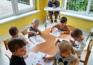 Dzieci z grupy Biedroneczki siedzące przy stole podczas malowania kredkami.
