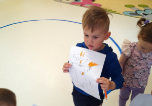 Tymon stojący wśród dzieci pokazuje pomalowany rysunek stracha.