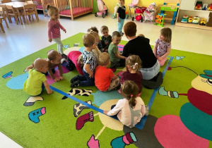 Dzieci z grupy Żabki wraz z opiekunką siedzą w środku kwadratu zrobionego z taśmy.