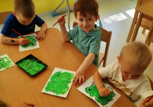 Dzieci siedzące przy stole malują na zielono szablony zwierzaków.