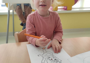Maria koloruje pomarańczową kredką obrazek przedstawiający łyżwiarkę.