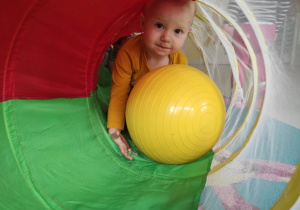 Zdjęcie uśmiechniętego Wiktora podczas pokonywania tunelu z żółtą piłką.