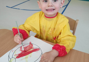 Hubert pozuje do zdjęcia malując swoją piłeczkę czerwoną farbą.