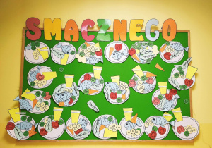 Zdjęcie tablicy grupy Pszczółki z ozdobionymi przez dzieci talerzykami różnymi produktami spożywczymi.