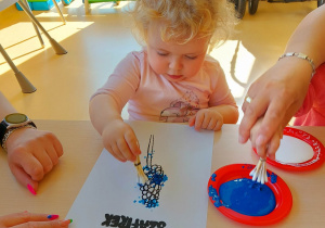 Laura starannie maluje swojego szafirka patyczkami do uszu namoczonymi w niebieskiej farbie.