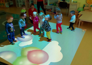 Zdjęcie dzieci bawiących się na dywanie przedstawiającym kolorowe baloniki.