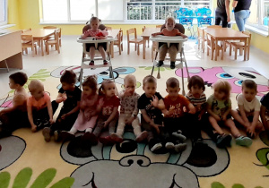 Zdjęcie dzieci siedzących na dywanie i oczekujących na gości.
