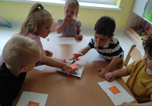 Henryk, Zuzanna i Wiktor biorą z papierowego talerzyka pomarańczowe kwadraty.