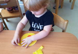 Kamilka przykleja kawałek żółtej bibuły do żólłtego koła z papieru.