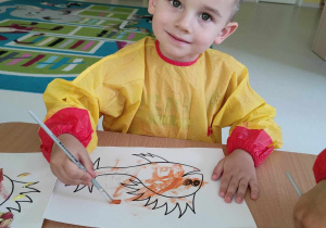 Uśmiechnięty Hubert pozuje do zdjęcia malując swoją rybkę na pomarańczowo.