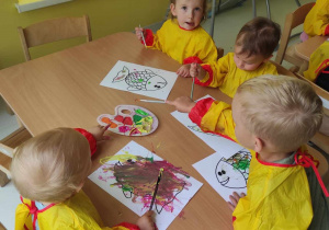 Zdjęcie dzieci siedzących przy stoliczku podczas malowania kolorowymi farbami swoich rybek.