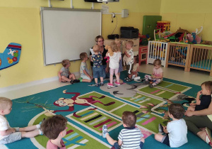 Zdjęcie dzieci i opiekunki z grupy Pszczółki przygotowujących się do zajęć na dywanie pt. ,,Gdzie możemy spędzać wakacje?''.