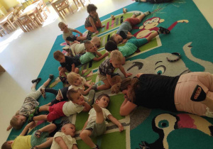 Dzieci i opiekunki leżą na dywanie podczas ćwiczeń relaksacyjnych.