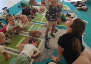 Dzieci i opiekunka rozciągają się na dywanie.