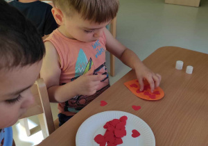 Nataniel przykleja na swojego pomarańczowego papierowego loda aplikację w kształcie czerwonego serduszka.