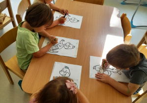 Dzieci malują na zielono szablon smoka.