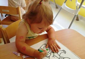 Lila zieloną kredką maluje swojego smoka.