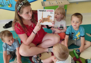 Zdjęcie opiekunki z grupy Pszczółki pokazującej dzieciom książeczkę pt. ,,Pierwsze czytanki dla...''.
