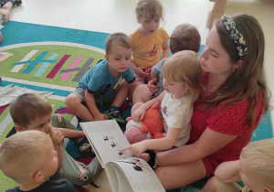 Zdjęcie opiekunki czytającej dzieciom na dywanie bajkę o sroczkach.