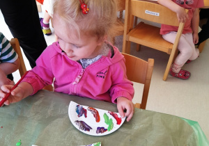 Kamila maluje kolorowymi farbami papierowy talerzyk.