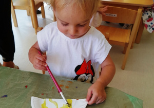 Aniela maluje papierowy talerz żółtą farbą.