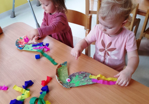 Dwoje dzieci przy stoliku wykonuje swoje kolorowe ptaki.