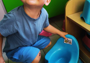 Uśmiechnięty Szymon pozuje do zdjęcia podczas przyklejania swojego obrazka na niebieski nocniczek.
