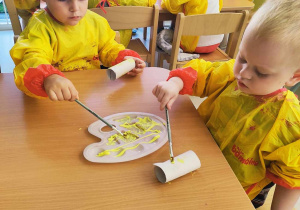 Hubert i Szymon malują żółtą farbą swoje tekturowe rolki.