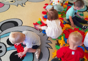 Dzieci z grupy Biedroneczki bawią się klockami na dywanie.