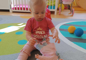 Zdjęcie Amelii siedzącej na dywanie podczas zabawy lalką.