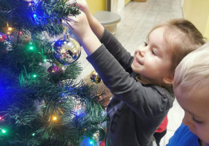 Hania zawiesza bombkę na świątecznym drzewku.