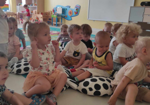 Zdjęcie słuchających dzieci, które siedzą na dywanie przed tablicą suchościeralną.