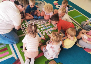 Zdjęcie dzieci i opiekunki na dywanie przygotowujących się do zajęć pt. ,,WAKACYJNE MEMORY''.