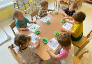 Dzieci siedzące przy stole podczas wykonywania zielonych żabek.