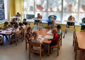 Dzieci z grupy Biedroneczki siedzące przy stole podczas malowania kredkami.