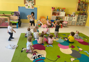 Opiekunka pokazuje dzieciom siedzącym na dywanie ilustracje w książce.