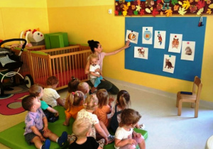 Dzieci obserwują opiekunkę, wskazującą na obrazki zwierząt domowych.