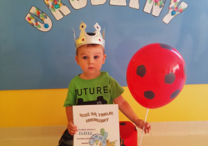 Zdjęcie chłopczyka z dyplomem i balonem w dniu urodzin.
