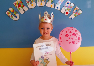 Dziewczynka w dniu swoich urodzin pozuje z balonem i dyplomem.
