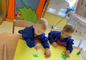 Dwoje chłopców odbijają swoje pomalowane rączki na wspólnym plakacie.