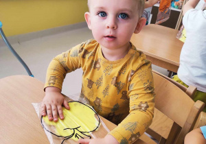 Szymon pozuje do zdjęcia trzymając w dłoni folię pomalowaną żółtą farbą.