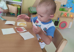 Zdjęcie Leona przyglądającego się układanym przez siebie obrazkom z kolorowymi jabłuszkami.