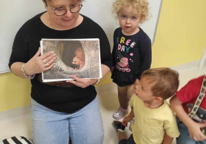 Opiekunka pokazuje dzieciom zdjęcie, w którym mieszka wiewiórka.