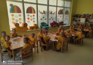 Zdjęcie dzieci z grupy Pszczółki siedzących przy stoliczku i przygotowujących się do zajęć plastycznych pt. ,,JESIENNE DRZEWKO''.