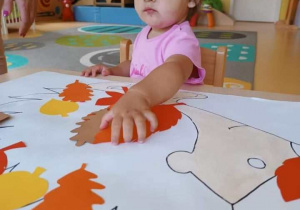 Laura przykleja na szablon jeża pomarańczowy liść.